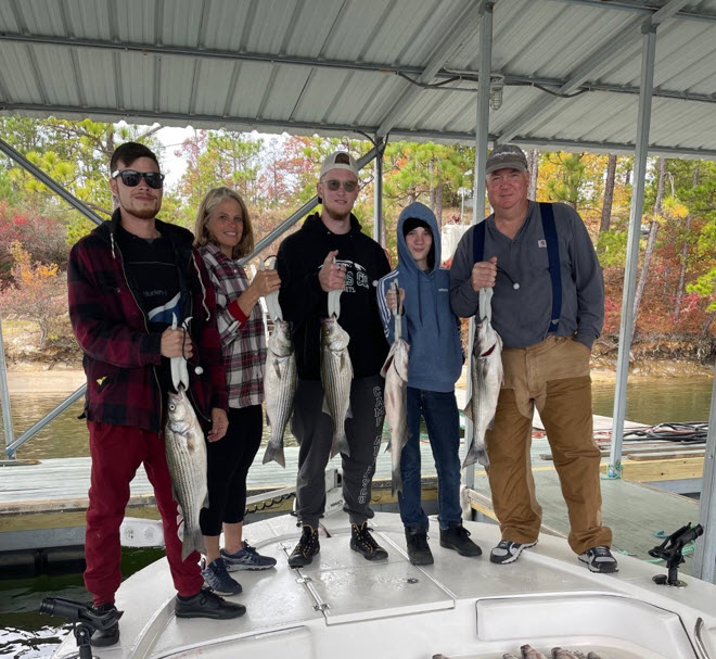 A group of five men and women pose while holding up fish they just caught