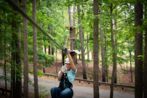 A woman smiling as she zip lines through the woods at Wind Creek State Park in Alabama